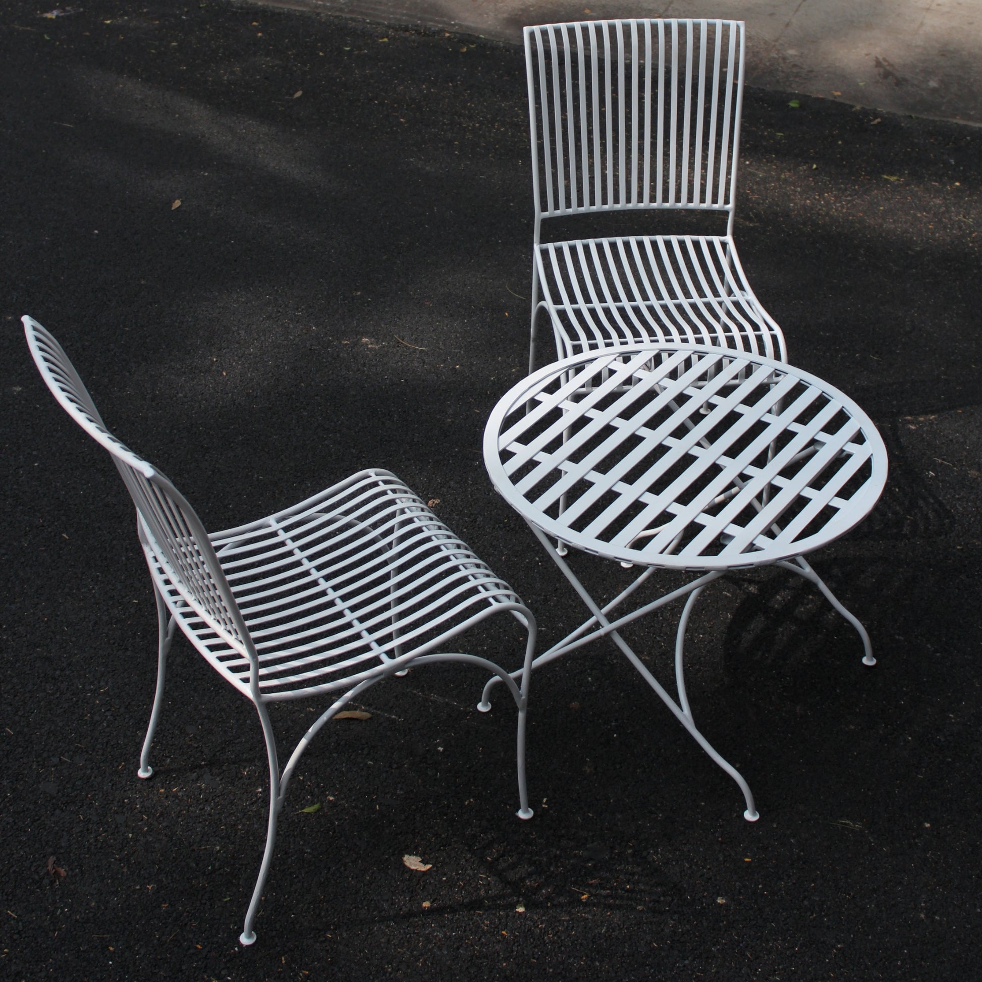 Angled view of white metal patio bistro table set with two matching chairs and round table