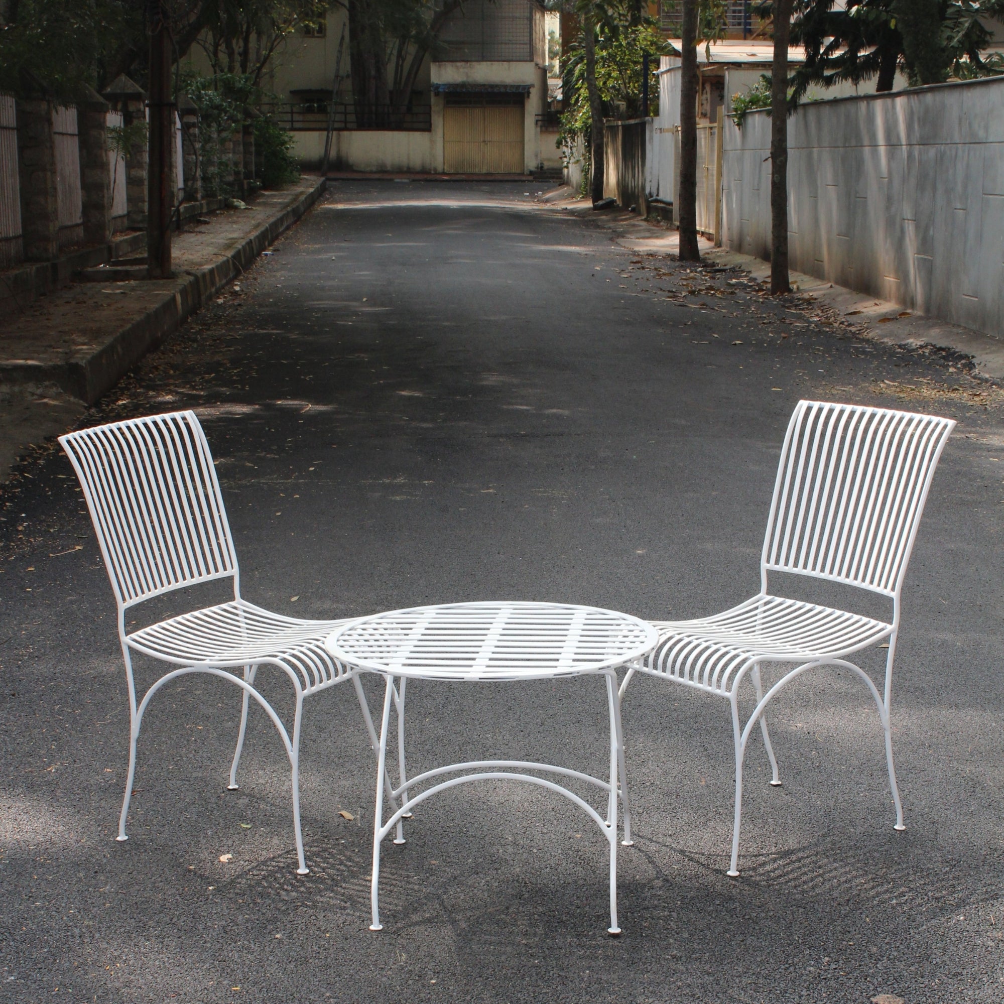 White metal outdoor bistro table set with two chairs placed on street showing full front view of garden seating set